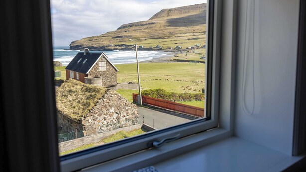 Ein Küstendorf mit Steinhäusern, einer Wiese und Blick auf das Meer durch ein Fenster.