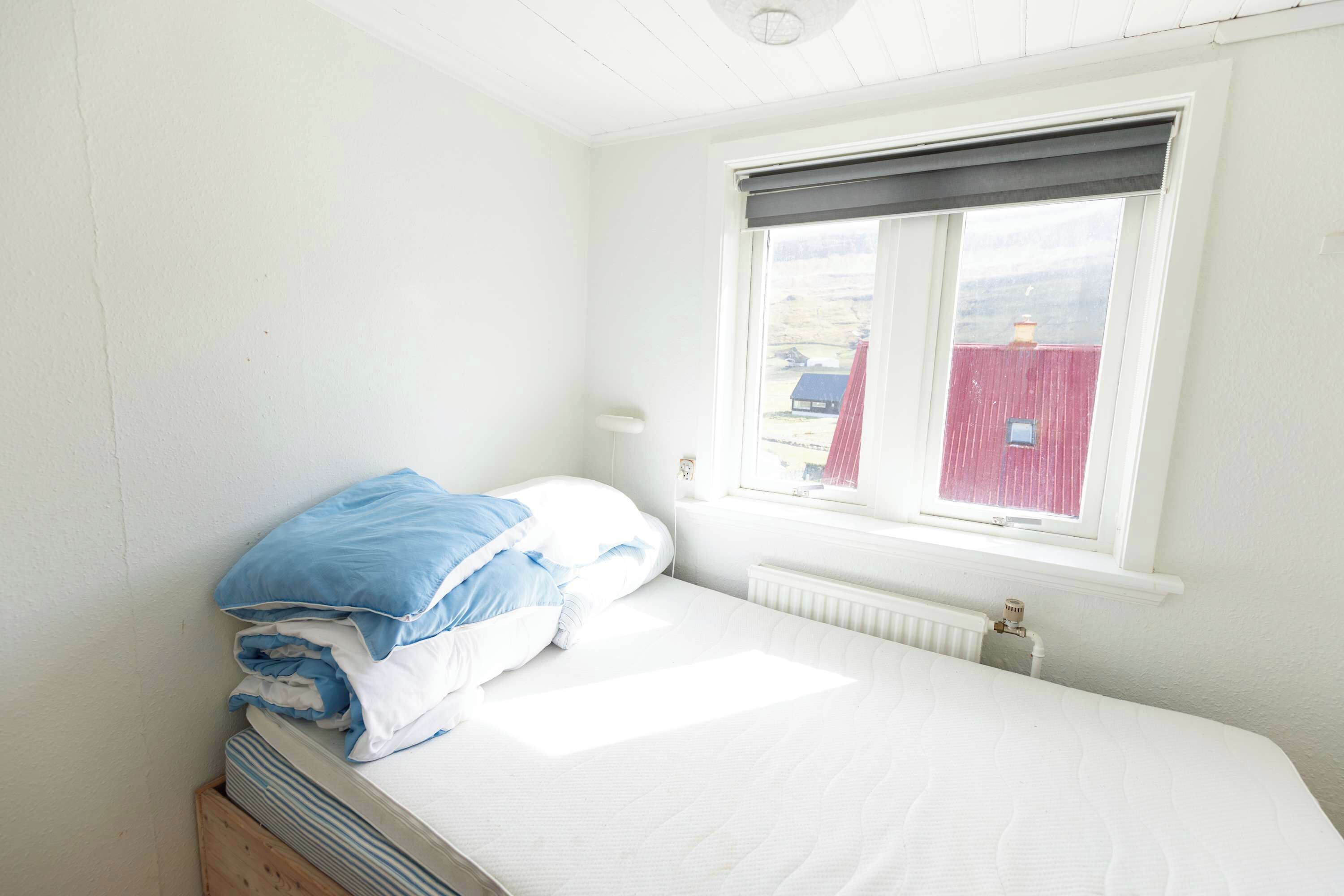 Une chambre individuelle avec un lit simple, une fenêtre, des murs blancs et un radiateur.