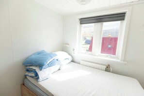 A single-bed room with a window, white walls, and a radiator.