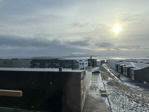 A view of a building complex with multiple structures, a parking area, and a body of water in the distance. - New Luxury Apartment With Panorama Views (Hoyvík)