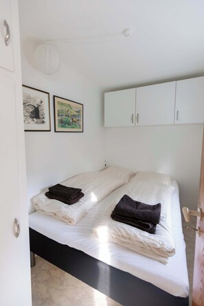 Ein Schlafzimmer mit einem Bett, zwei gerahmten Bildern, einem weißen Kleiderschrank und einer Tür.