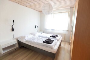 Ein Schlafzimmer mit einem Bett, einem Nachttisch, einer Lampe und einem Fenster mit Vorhängen.