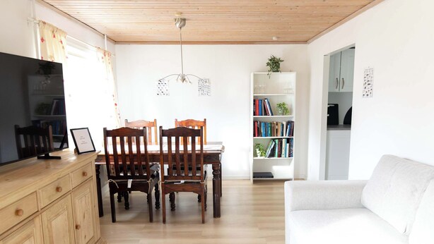 A modern living room with a wooden dining table, chairs, a white sofa, and a bookshelf. - Cozy Apartment in the Heart of Torshavn - 6 Sleeps (Tórshavn)