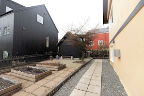 Ein Innenhof mit erhöhten Blumenbeeten, einer Bank und einem Weg zu einem Gebäude mit roter Fassade.