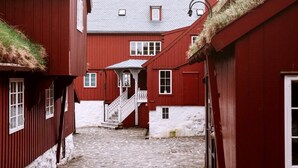 A narrow cobblestone alley between red buildings with white walls and a staircase leading to a second floor. - Cozy Apartment in the Heart of Torshavn - 6 Sleeps (Tórshavn)