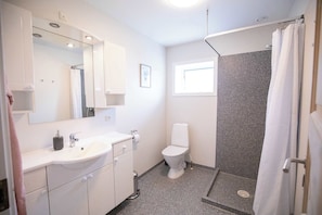 A bathroom with a white sink, mirror, and toilet, a shower with a curtain, and a window providing natural light. - Torshavn Home with Views Near City Center (Tórshavn)