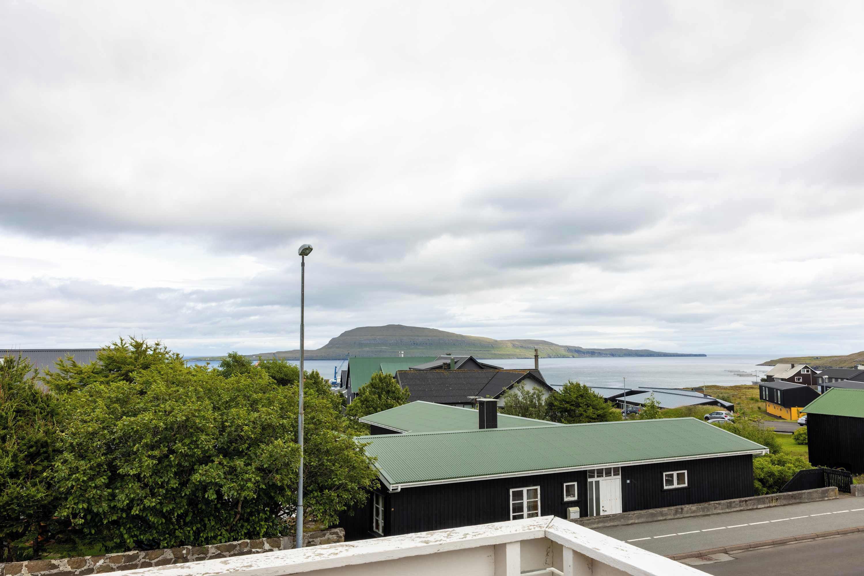 A coastal residential area with houses, a street, and a view of the sea and hills.