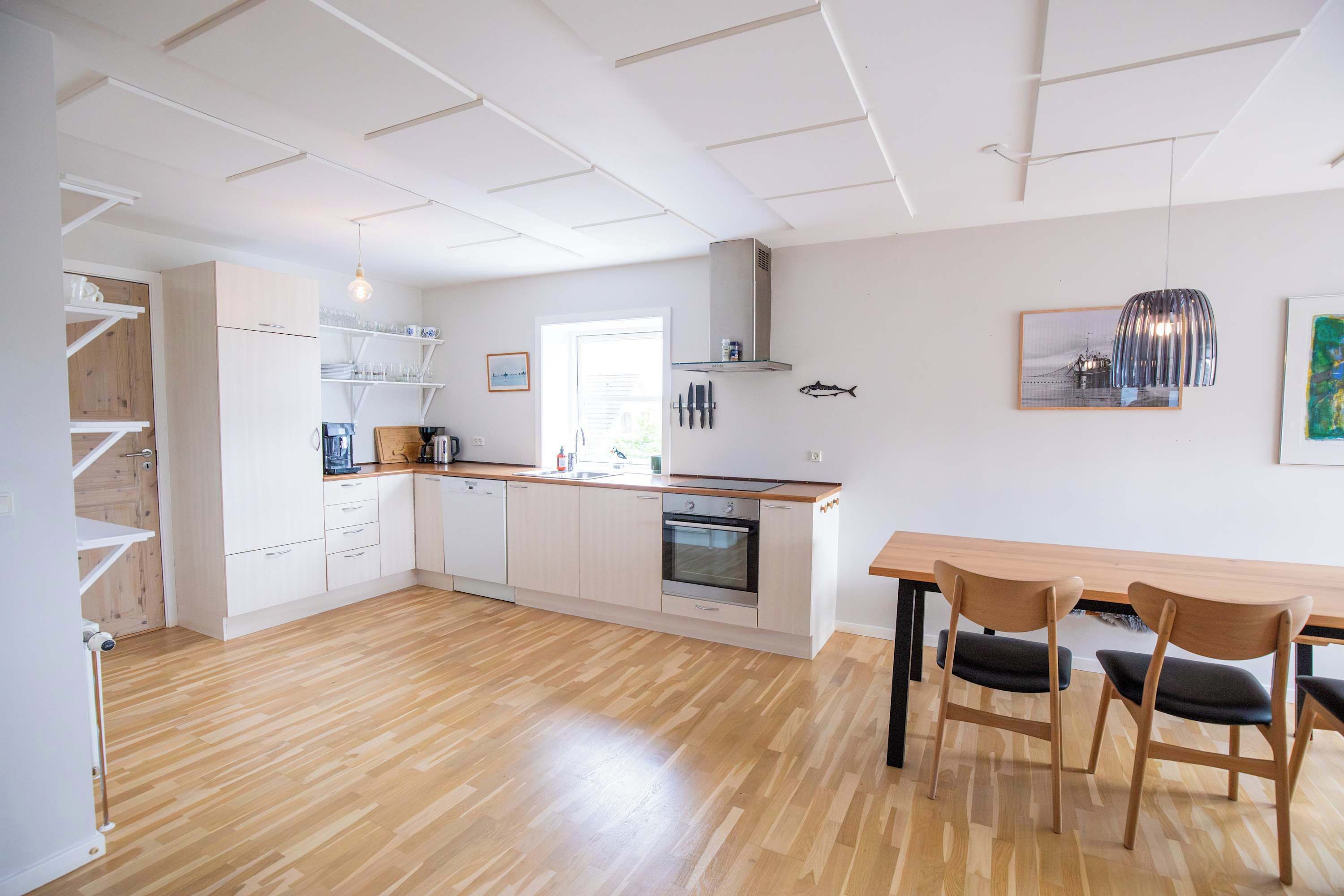 A modern kitchen with white cabinetry, a built-in oven, and a dining area with a wooden table and chairs.