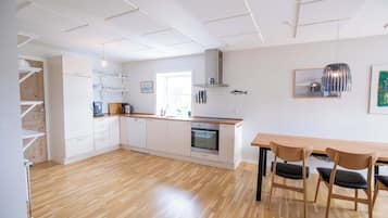 Una cocina moderna con armarios blancos, horno empotrado y comedor con mesa y sillas de madera.