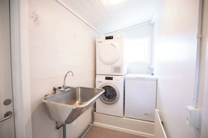 A laundry room with a sink, two stacked washing machines, and a window. - Torshavn Home with Views Near City Center (Tórshavn)