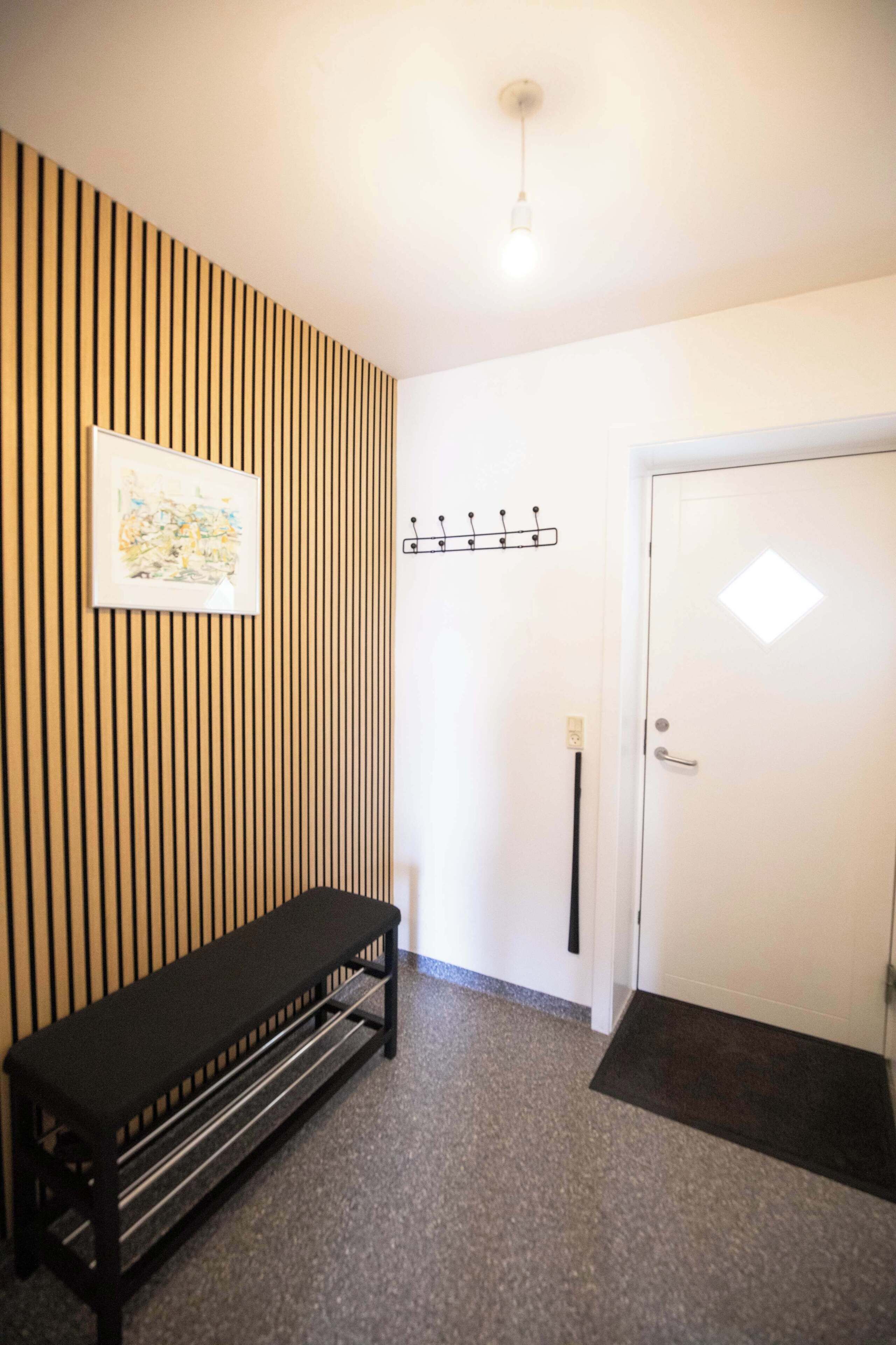 A hallway with a bench, a coat rack, and a door.