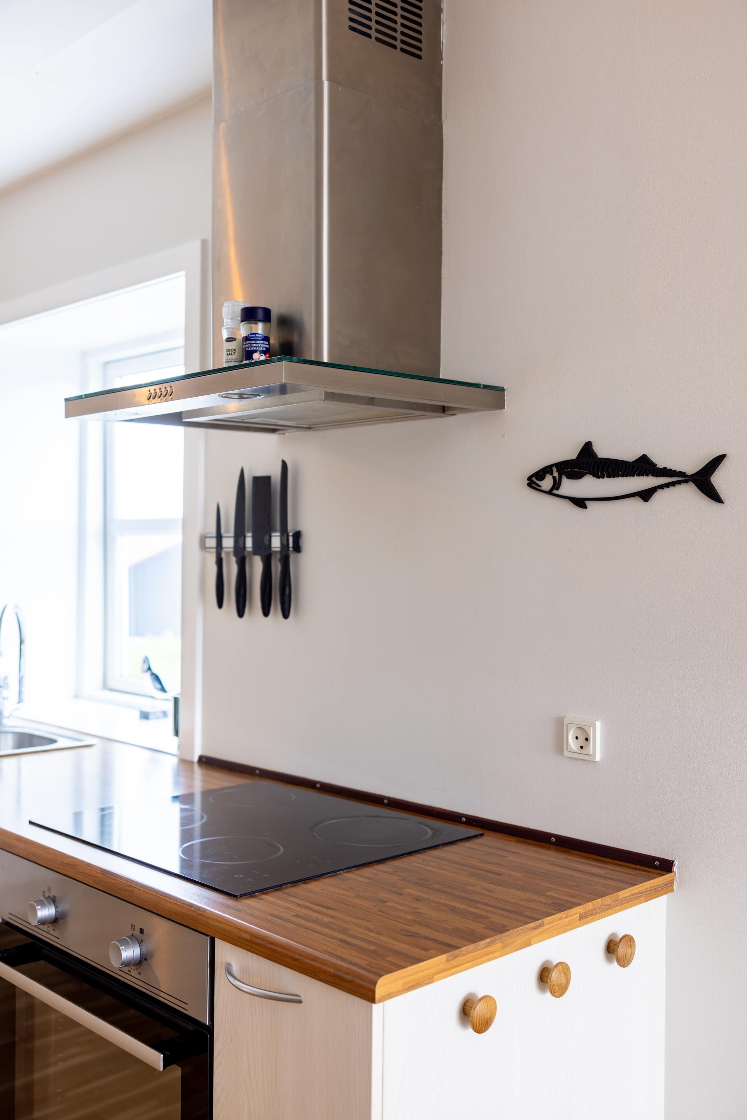 A kitchen with a stainless steel range hood, a fish decoration, and a knife rack.