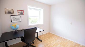 Une pièce avec un plancher en bois, un bureau noir surmonté d’un globe terrestre, une chaise et une fenêtre donnant sur un paysage verdoyant.