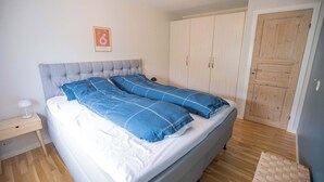 Um quarto com uma cama, mesa de cabeceira, guarda-roupa e uma porta.
