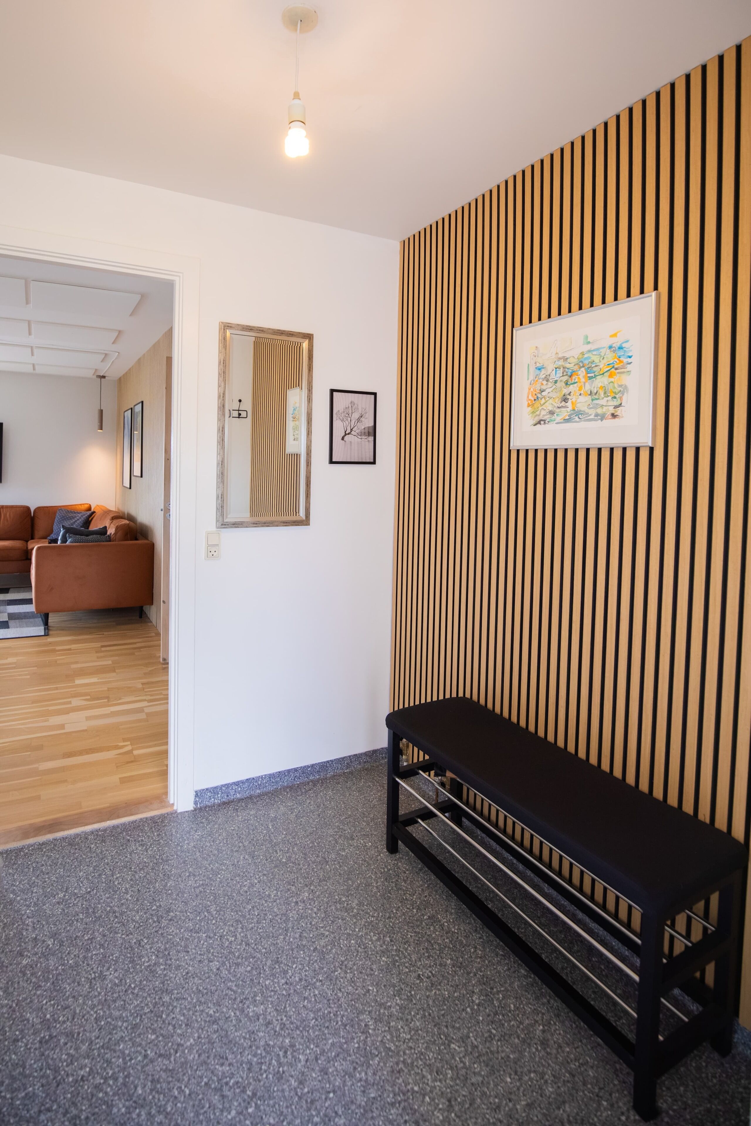 A modern interior with a bench, a framed artwork, and a mirror on the wall.