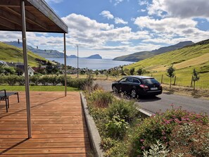 Une voiture est garée sur une route, avec une terrasse en bois et de la verdure au premier plan.