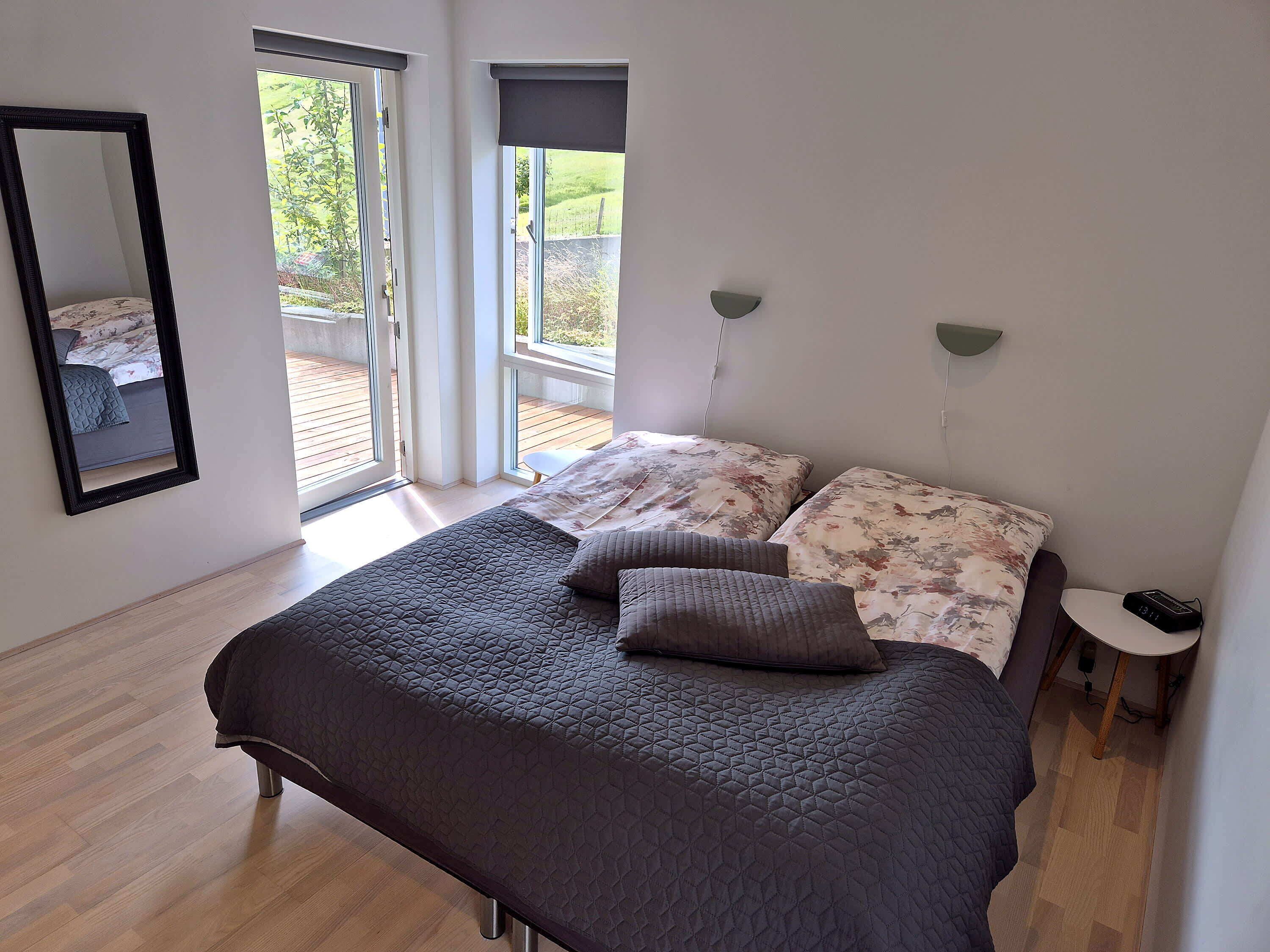 Un dormitorio con cama, mesita de noche, espejo y ventana con vistas a zonas verdes.