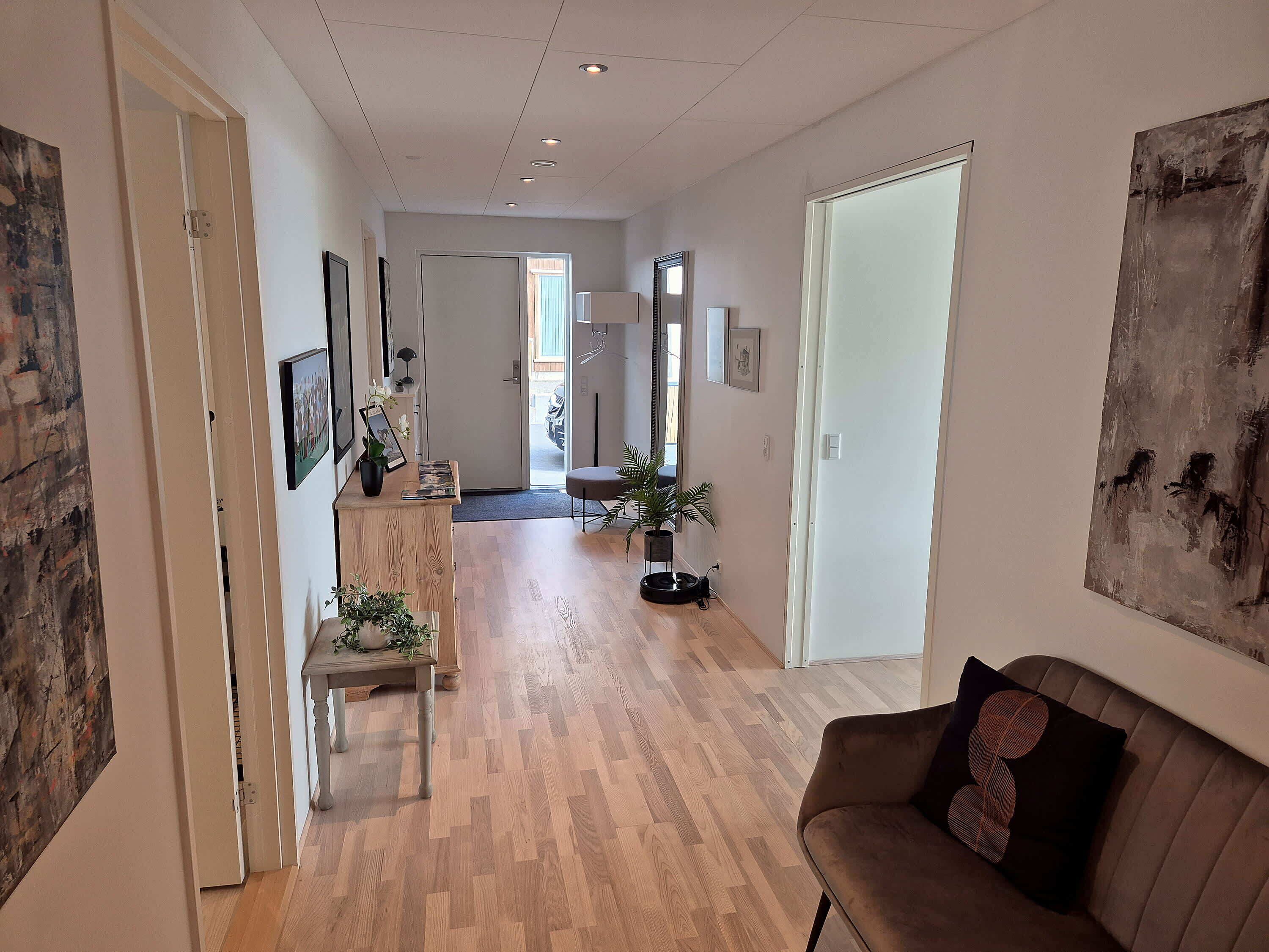 A hallway with a wooden floor, a reception desk, a couch, and a door leading to another room.