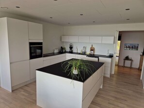 Une cuisine moderne avec des meubles blancs, un îlot central doté d’un plan de travail noir et un plancher en bois.