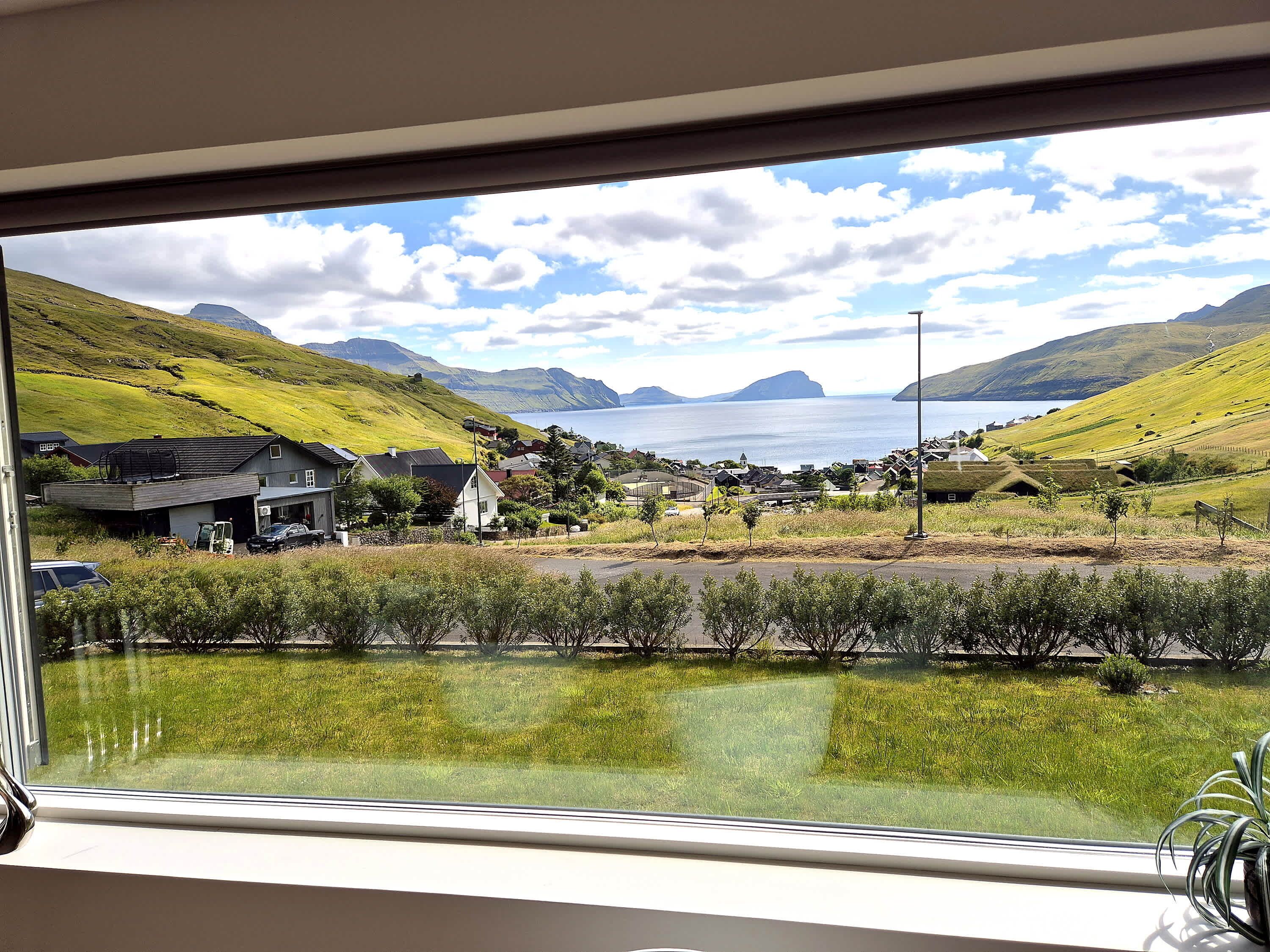 A view from a window overlooking a coastal village with houses, a road, and a body of water.