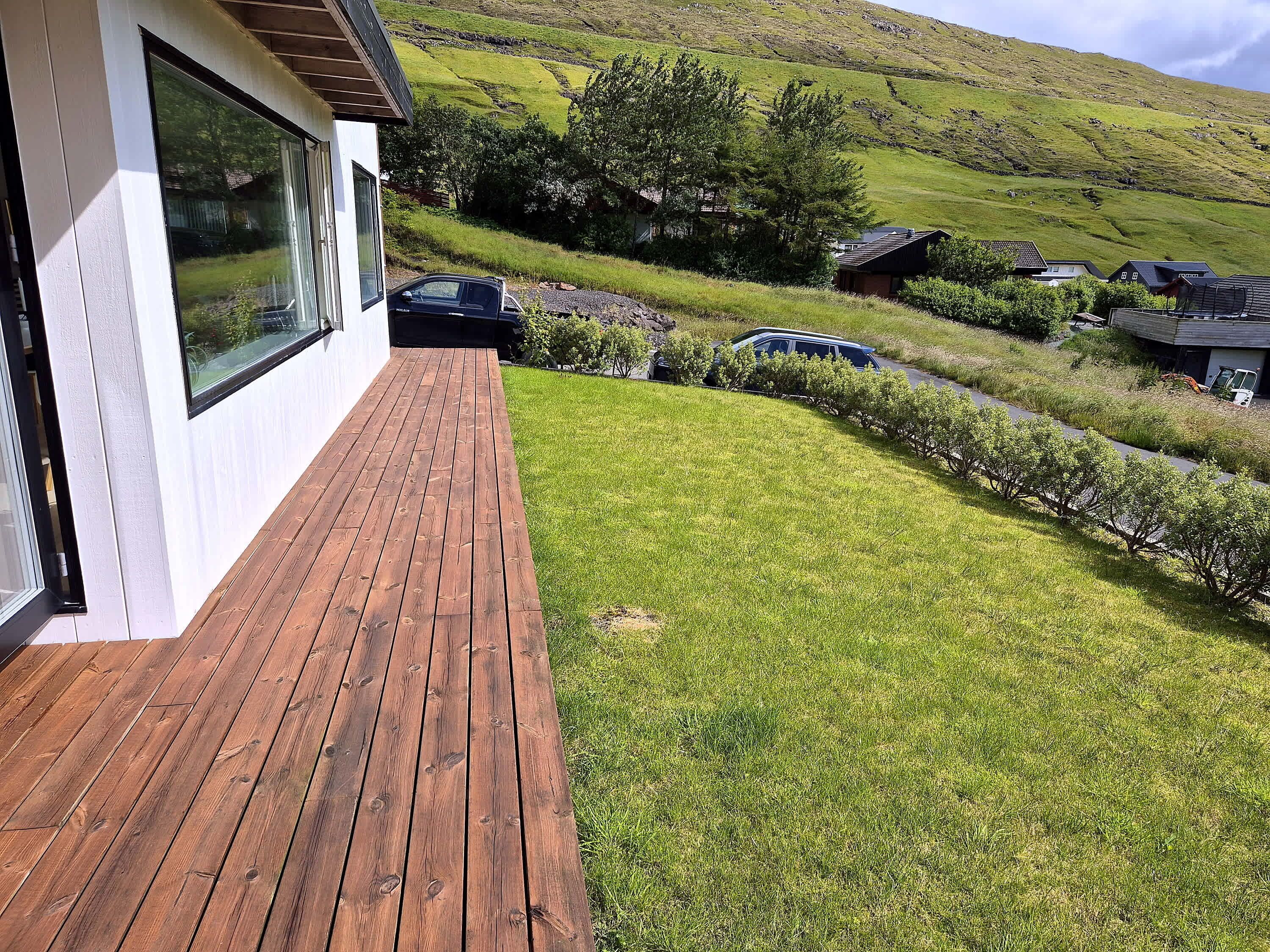 A modern house with a wooden deck, a grassy yard, and a view of a hilly landscape.