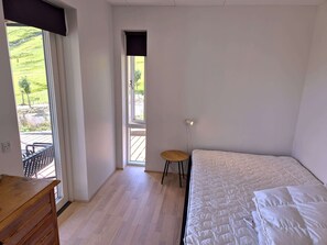 A bedroom with a bed, a small stool, and a view of a garden through a window. - Panoramic Fjord Views in Modern Kvivik House (Kvívík)