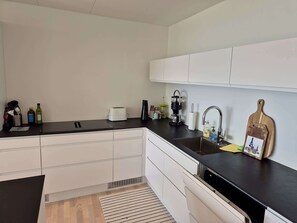 A modern kitchen with white cabinets, a black countertop, and a stainless steel sink. - Panoramic Fjord Views in Modern Kvivik House (Kvívík)