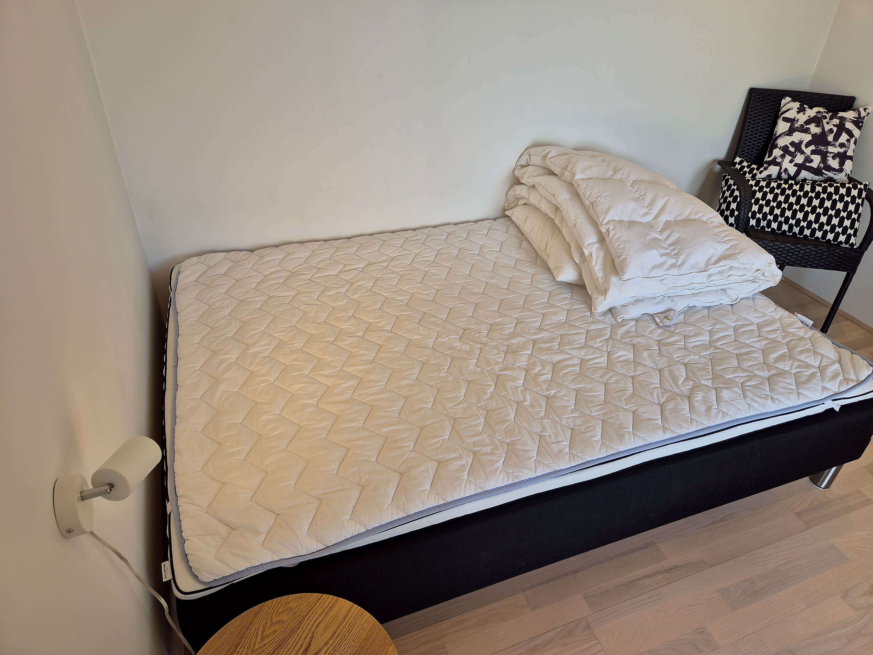 A bed with a quilted mattress, a black headboard, and a small round table beside it.