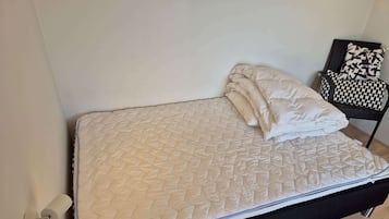 A bed with a quilted mattress, a black headboard, and a small round table beside it.