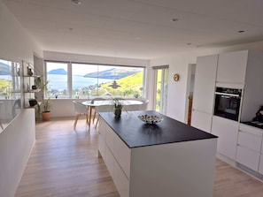 A modern kitchen with a central island, large windows, and a view of the landscape. - Panoramic Fjord Views in Modern Kvivik House (Kvívík)