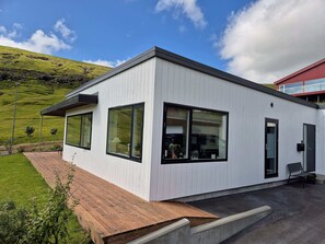 A modern building with large windows and a flat roof, situated on a grassy hill with a clear sky. - Panoramic Fjord Views in Modern Kvivik House (Kvívík)