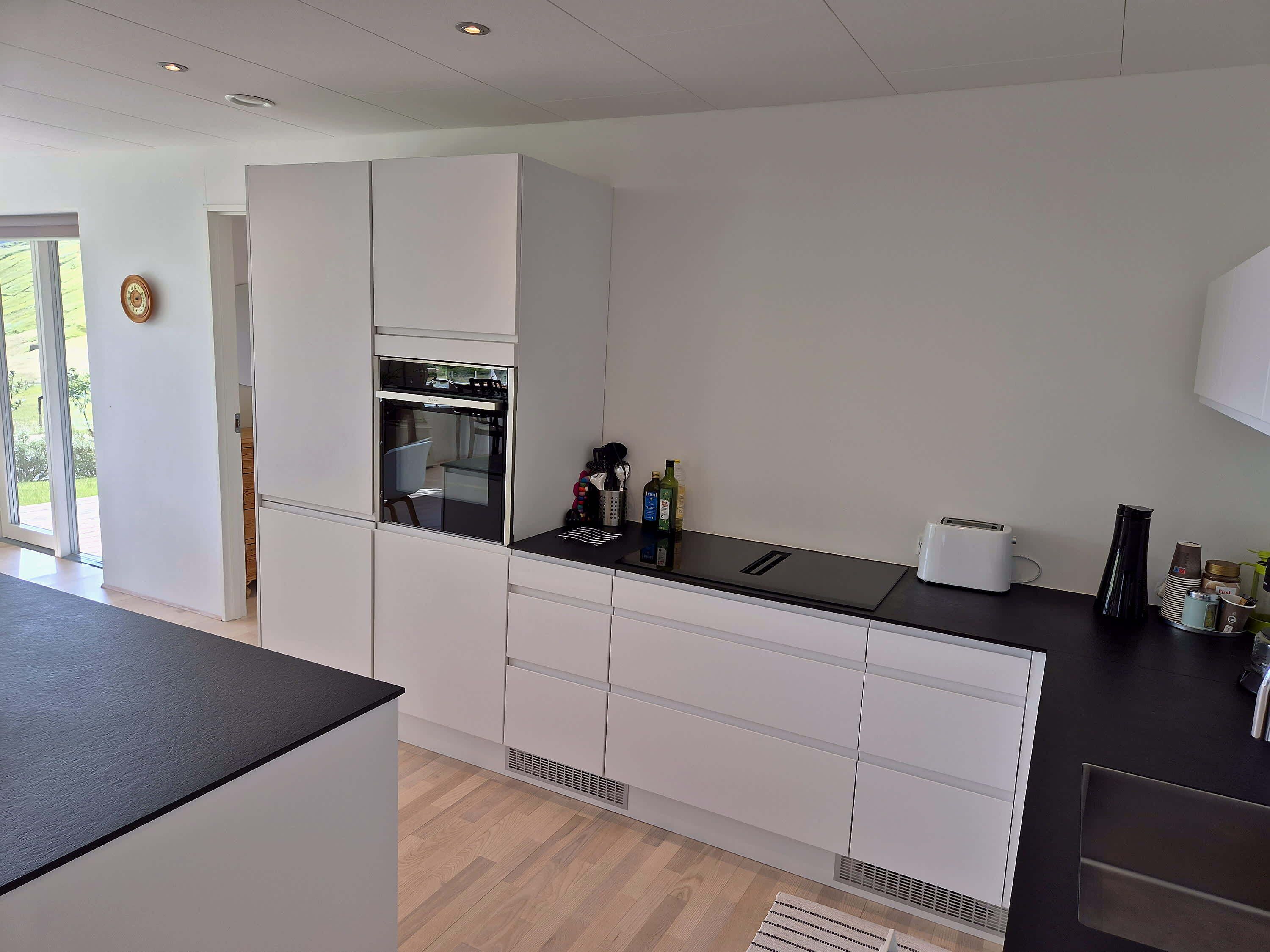 A modern kitchen with built-in appliances, a black countertop, and a view of the outdoors.