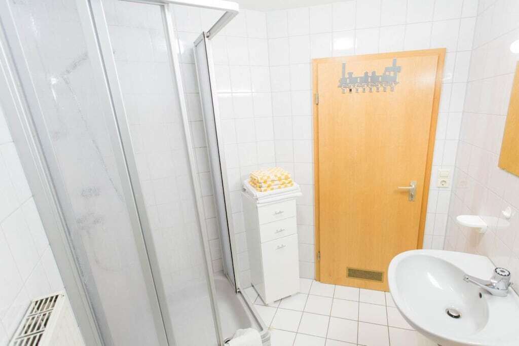 Une salle de bain avec une douche, un lavabo et une porte en bois ornée d’un motif représentant un paysage urbain.