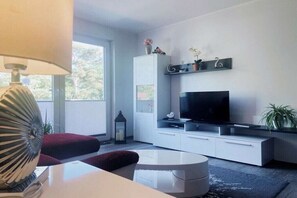 A modern living room with a flat-screen TV, white cabinets, a red ottoman, and a round coffee table. - Holiday apartment with 2 bedrooms (Dierhagen)