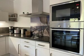 A modern kitchen with stainless steel appliances, including a built-in oven and microwave, and a black countertop. - Holiday apartment with 2 bedrooms (Dierhagen)