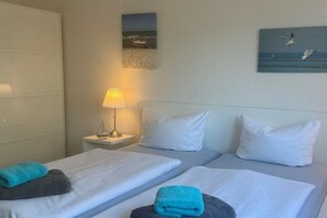 A hotel room with two beds, a nightstand with a lamp, and artwork on the walls. - Holiday apartment with 2 bedrooms (Dierhagen)