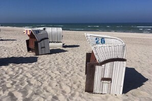 Sillas de playa con números, dispuestas en una playa arenosa con el océano al fondo.