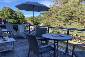 Una terraza con mobiliario exterior, incluyendo sillas y una mesa, además de un parasol grande.
