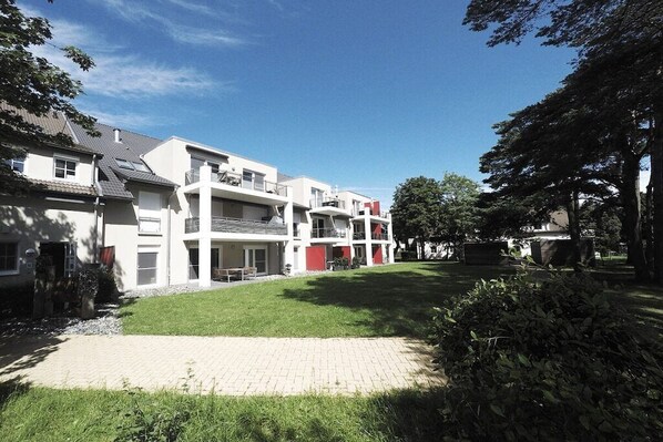 Un edificio residencial con varios pisos, un camino pavimentado y un césped bien cuidado.