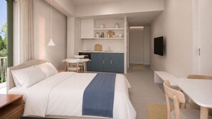Una habitación de hotel moderna con una cama grande, un escritorio, una kitchenette y un televisor montado en la pared.
