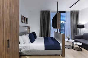 Una habitació d'hotel moderna amb llit, sofà, taula petita i televisió.
