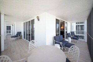 Een overdekt terras met een ronde tafel en stoelen, een glazen deur en uitzicht op het interieur.