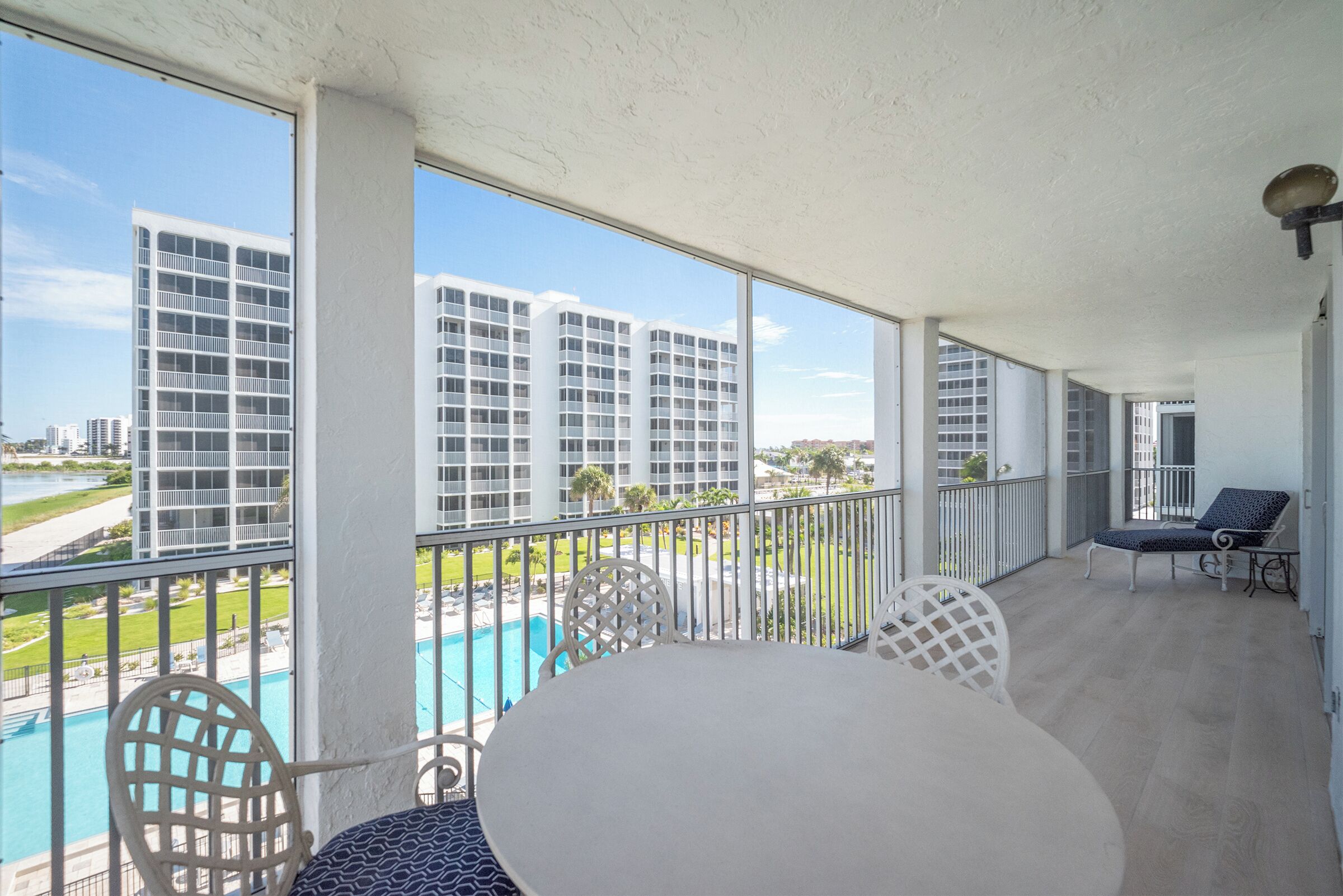 A balcony with a pool, white furniture, and a view of high-rise buildings.