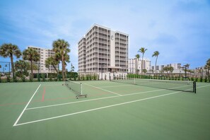 Een tennisbaan met net, omringd door palmbomen en gebouwen.