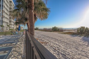 Ein Strand mit einer Palme, einem Zaun und einem Gebäude im Hintergrund.