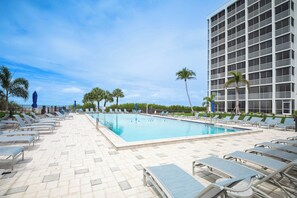 Área de piscina com espreguiçadeiras e um edifício com várias varandas.