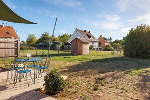 A wooden deck with metal chairs and a table, a small stone structure, and a fenced area with grass. - Holiday Home 'L'ancien Atelier' with Private Terrace, Wi-Fi and Air Conditioning (Muides-sur-Loire)