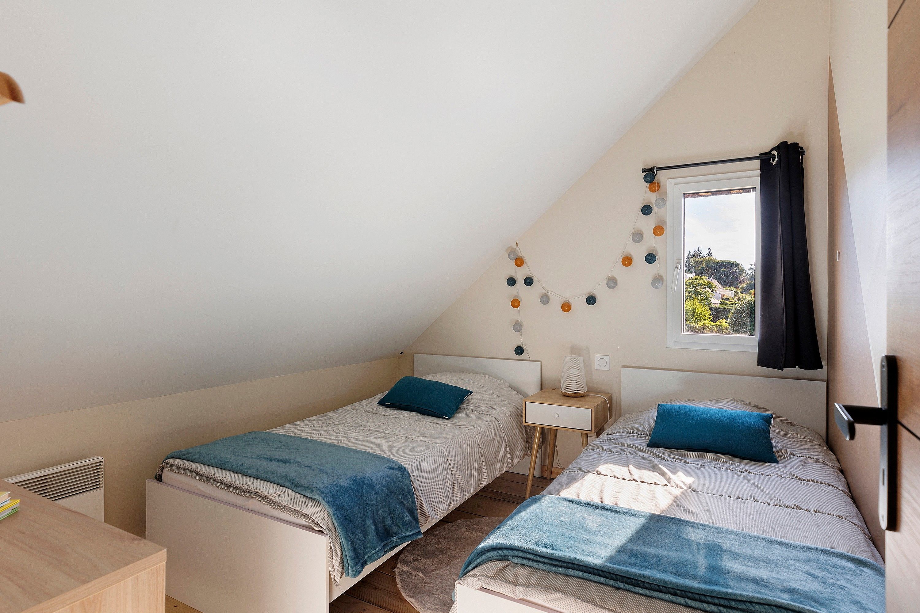 Une chambre avec deux lits, une fenêtre donnant sur un beau paysage, une table de chevet avec une lampe et un élément décoratif mural.