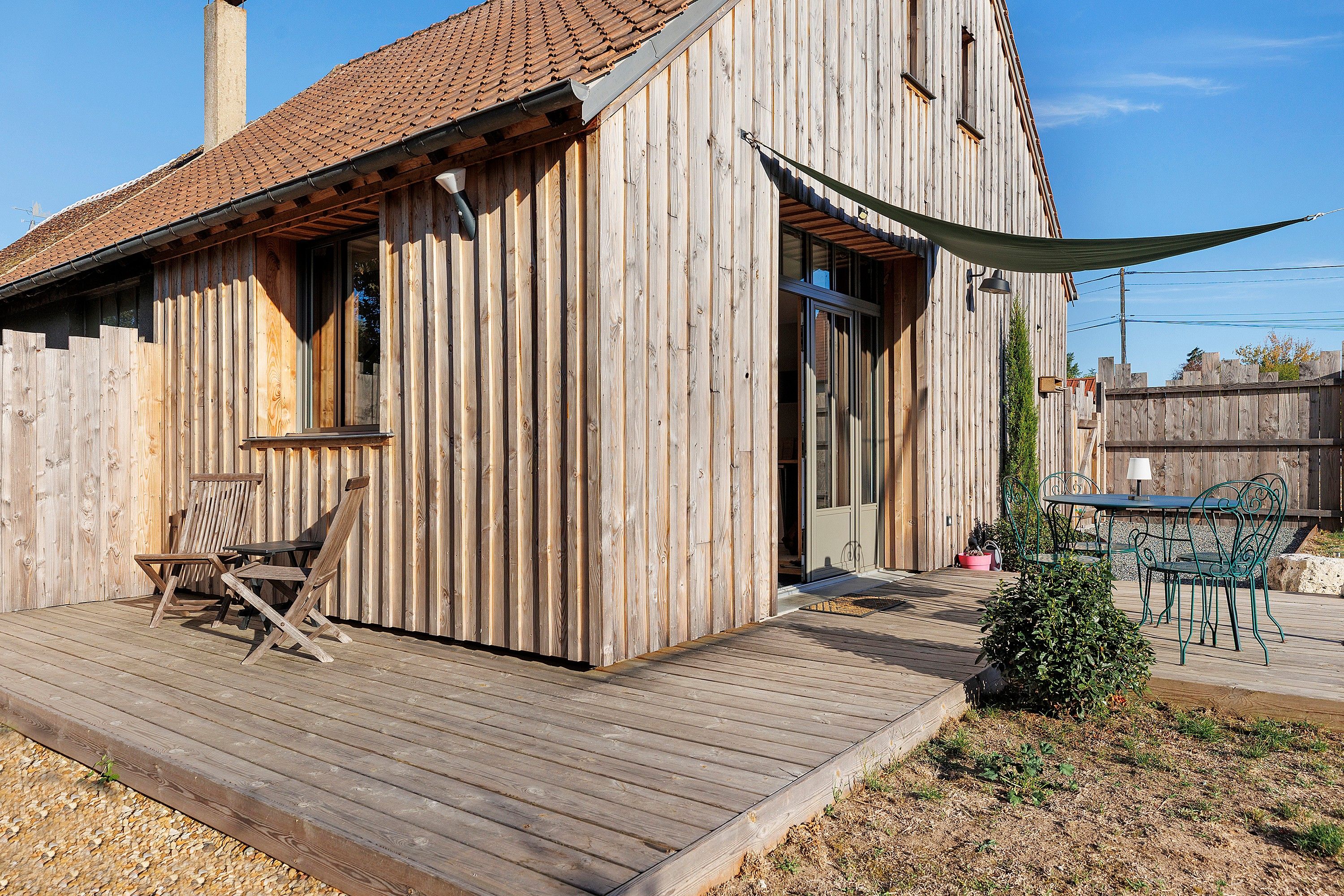 A wooden cabin with a deck, a small table, and chairs.