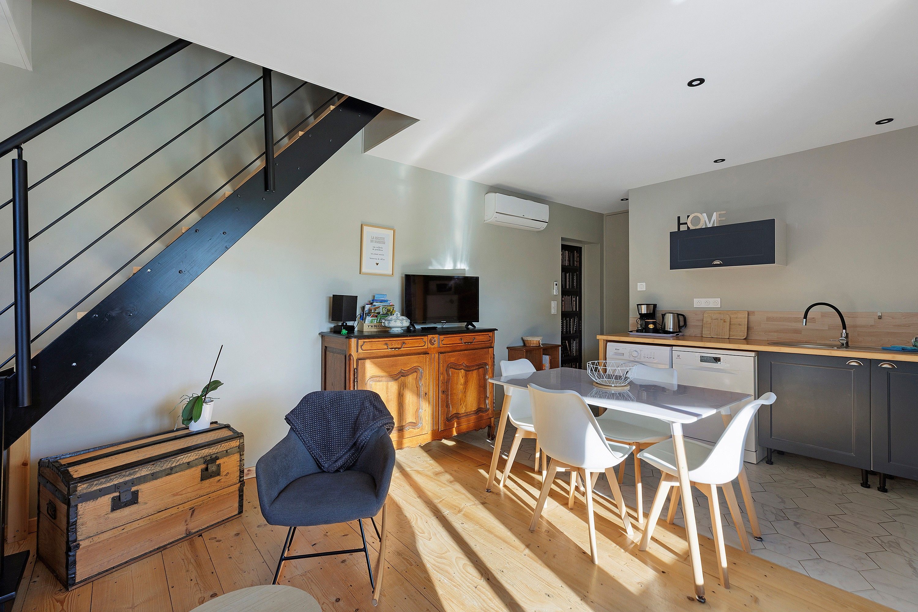 Una cocina moderna con comedor, piso de madera, una escalera y un televisor de pantalla plana montado en la pared.